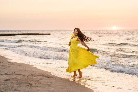 A girl of size L with black long hair is dancing on the seashore at dawn.
