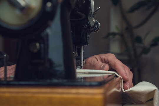 senior tailor working on vintage sewing machine on wooden table closeup