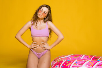 Pensive young blonde woman girl posing isolated on yellow background. People summer vacation rest lifestyle concept. Hold swim inflatable ring, biting lips looking aside