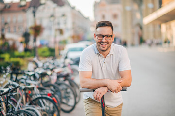 Close-up portrait of a happy man standing on a kick scooter on a sunny day.