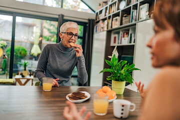 Two women talking and eating cookies at modern house.