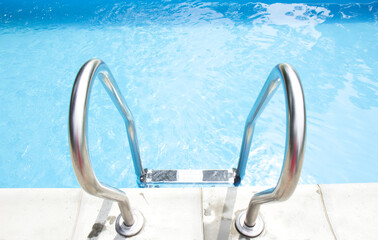 Swimming pool with stair. Clear and blue, clear water in the pool. Grab bars ladder in the blue swimming pool. Side view