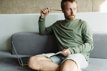Fototapeta premium Photo of thinking man working with laptop and writing down notes