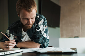 Photo of pleased man working with laptop and writing down notes