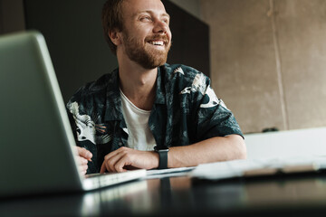 Photo of laughing man working with laptop and writing down notes