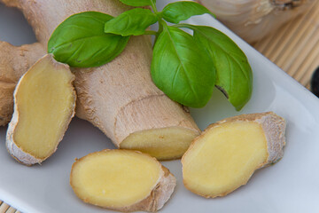 Ingwerwurzel, Ingwerscheiben auf einer weissen Schale mit Knoblauch und Basilikum