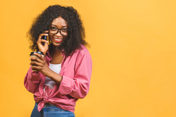 Portrait of african american woman 20s with afro hairdo looking aside while drinking takeaway coffee or tea from paper cup isolated over yellow background. Using phone.