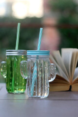 Two cactus shaped bottles with cold water and open book in a garden. Selective focus.