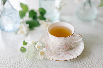 Obraz na płótnie Canvas White blossom jasmine flowers in vase on the table with a cup of tea
