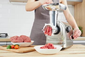 Foto auf Acrylglas Raw meat. The process of preparing forcemeat by means of a meat grinder. Female hands use meat chopper at kitchen. © wertinio