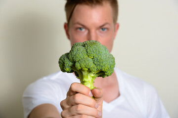 Fototapeta na wymiar Portrait of young handsome man giving broccoli