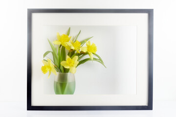 Home interior floral decor. Frame decorated flowers in vase on white table. Poster with narcissus on color background.