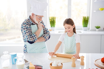 Photo of little girl granddaughter passing examination aged chef grandpa looking attentively forming dough rolling pin baking cookies weekend home kitchen indoors