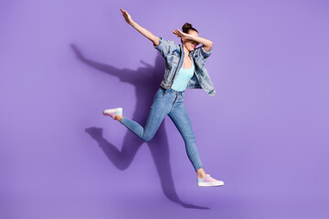 Fototapeta na wymiar Full size photo of pretty youth girl jump dance hip-hop dab close cover face arms wear denim jacket singlet glasses sunglasses isolated over purple color background