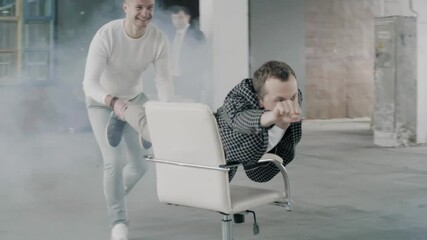 The manager in the office rolls a colleague on a chair like Batman. Office staff having fun. - Powered by Adobe