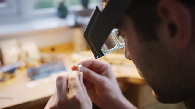 Pull focus close up of male jeweller looking at ring through headband magnifiers in studio - shot in slow motion 