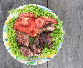 Fried pork with tomatoes laid on lettuce on a colored plate. View from above. Close-up.
