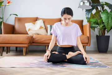 Obraz premium beautiful asian-looking girl sitting on a carpet in a sports uniform at home in lotus position