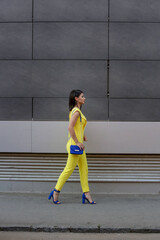 Outdoor portrait of young fashionable woman wearing a yellow jumpsuit and blue accessories