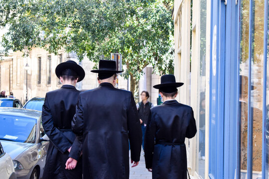 Three Hasidic Jewish men walk at a public street in Paris, France. Jewish or Judaic religious clothing. 