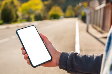 A teen boy holds a smartphone in his hand. Blurred empty street on the background. Close up. Mock up. The concept of communication and modern technologies