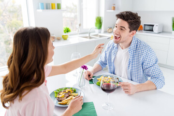 Portrait of his he her she two nice attractive lovely careful cute positive cheerful cheery spouses eating tasty fresh meal dish feeding each other in light white interior kitchen house apartment