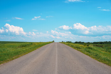 Highway in the middle of green picturesque fields against a blue sky with clouds.