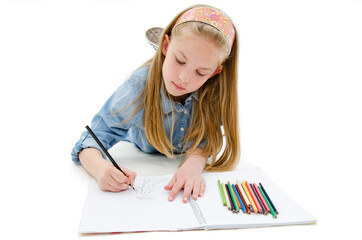 Pretty happy little girl lying and drawing with pencils. Isolated on white background