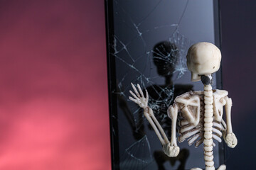 the human skeleton looks in dark glass with cracks and is surprised. toy skeleton by the mirror