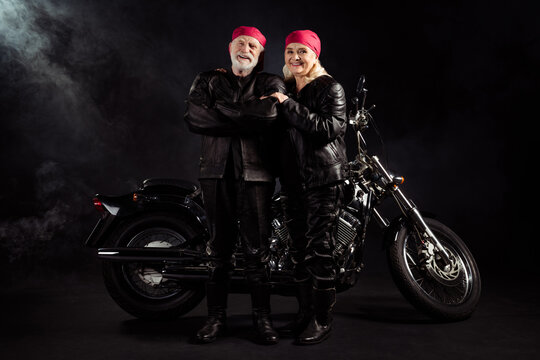 Full length photo of aged bikers grey hair man lady couple drive vintage chopper traveling together feel young rock moto festival wear rocker leather outfit isolated black color background