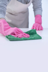Young woman housekeeper in apron is wearing pink gloves to clean the table, concept of preventing virus infection, housekeeping service, close up.