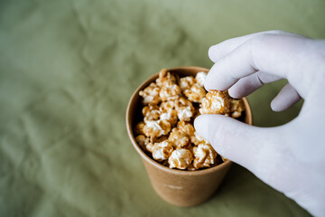 a hand takes sweet popcorn from a brown jar, a box of popcorn on a colored background, a gloved hand reaches for fast food, a minimalistic concept
