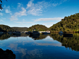 Beautiful morning view of Creek with boats and reflections of blue sky, light clouds, mountains and trees. Berowra Waters, Berowra Valley National Park, New South Wales, Australia