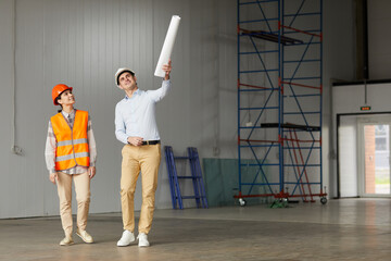 Engineer in work helmet pointing at something and explaining the process of work to worker they standing in empty building