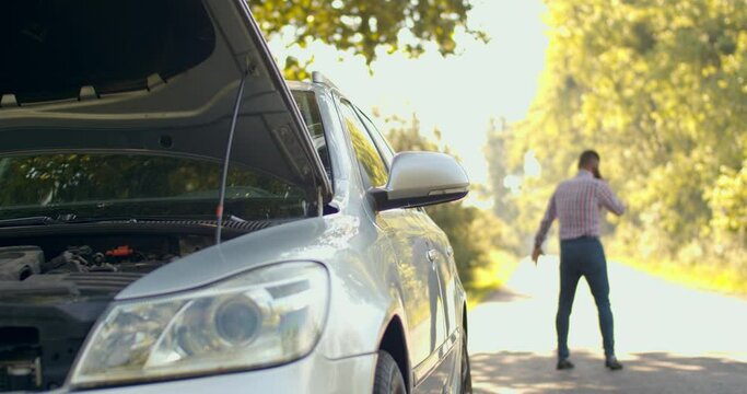 Caucasian man standing near broken car calling for repair service help. emergency light, engine problem, worried. Car accident. Car trouble. medium shot slow motion