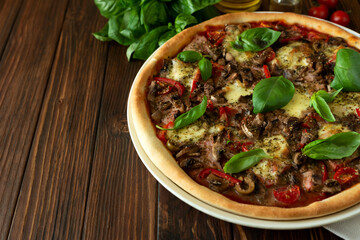 Delicious Italian pizza and cherry tomatoes and basil on brown wooden background. Copy space.