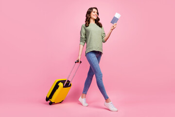 Full length profile side photo of positive cheerful girl hold tickets carry suitcase go walk first-class check-in plane wear good look pullover footwear isolated over pastel color background