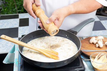 Chef putting pepper in the pan for cooking mushroom cream soup