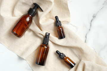 Set of cosmetic amber glass bottles with beige fabric on marble table. Flat lay, top view. Beauty...