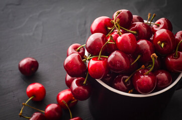 Ripe red cherries in a bowll on black stone background. Fruits healthy food