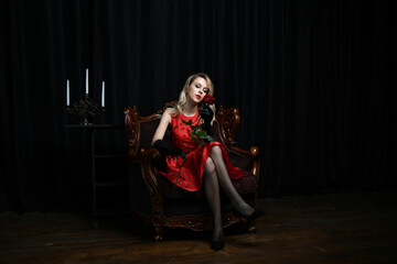 Fototapeta na wymiar beautiful girl in a red dress posing in a chair with a red rose on a black background