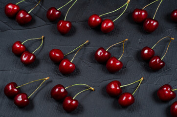 Creative fresh cherry pattern background with copy space. Top view. Sprinkled cherry on black stone background.