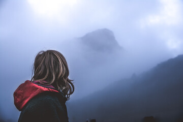 Chico de pelo largo en primer plano adentrándose en un paisaje de nieblas y montañas en silueta