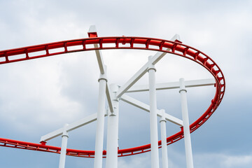 Red roller coaster in the amusement park, the background is a blue sky with white clouds