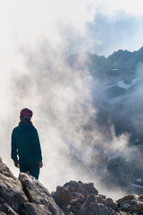 Montañero contemplando el paisaje entre las nubes iluminadas y un fondo montañoso