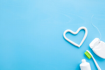 Toothbrush, white tube of toothpaste, container of dental floss on blue table background. Pastel...