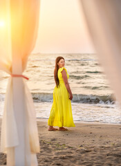 Girl size with black long hair and a long yellow dress walking on the seashore at dawn.
