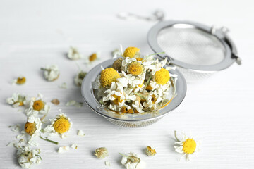 Dry chamomile flowers in infuser on white wooden table, closeup