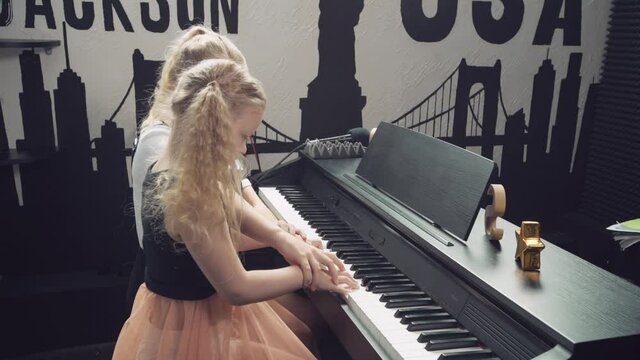 Two cute blonde girls with blond eyes setra play the piano together.