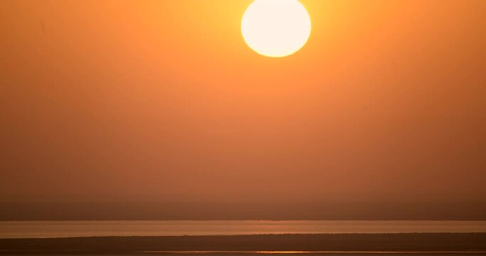 Distorted sun sphere raising from the hot desert haze in a time-lapse. 4K beautiful sunrise.